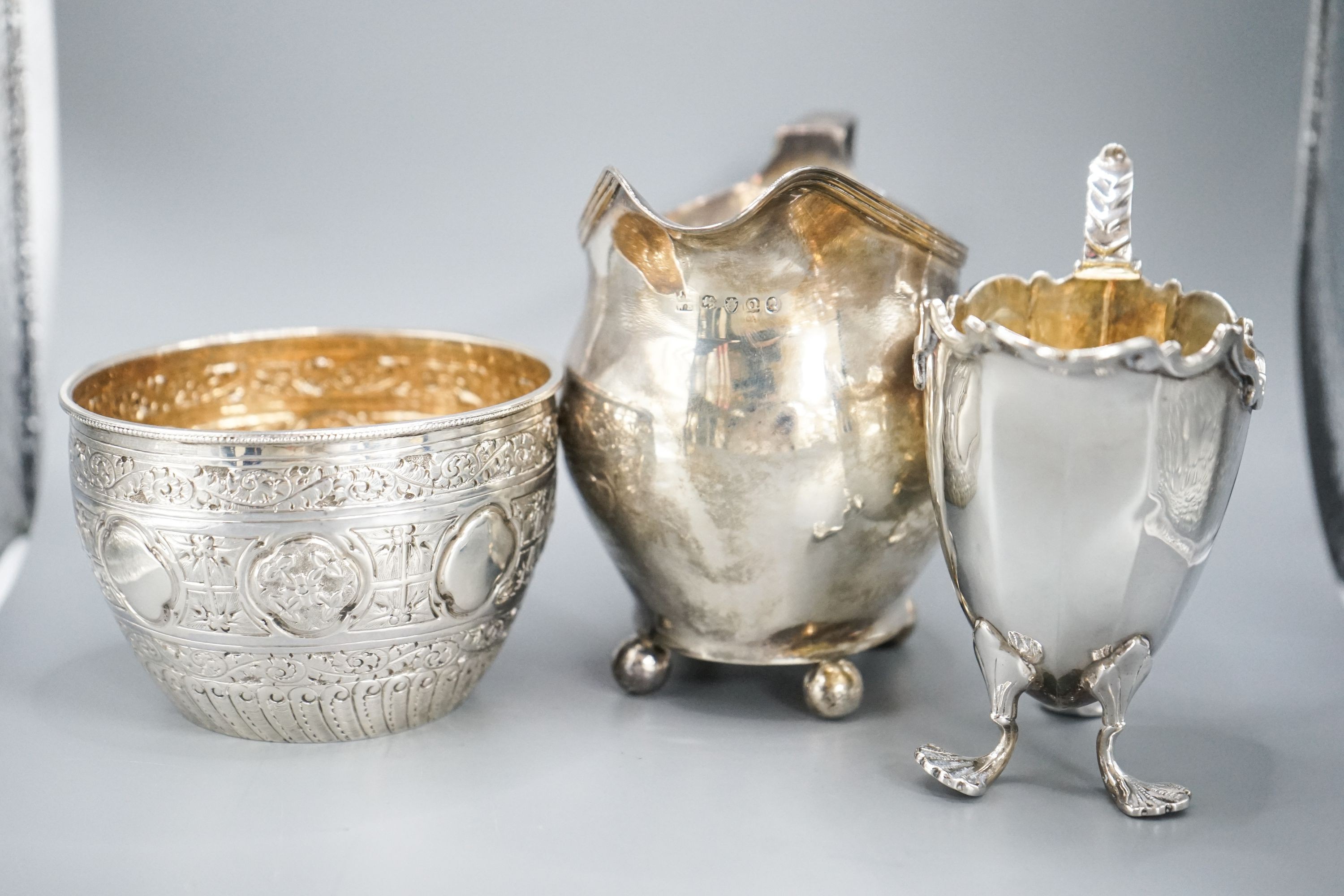 A Victorian repousse silver sugar bowl, a George III silver cream jug and a later silver cream jug